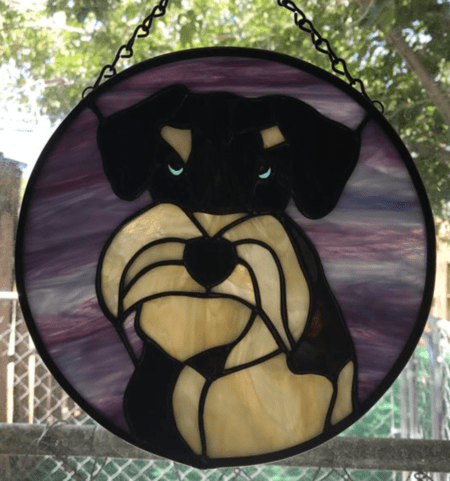 A stained glass dog sitting in front of a fence.